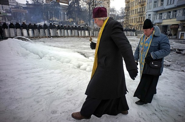 : Priests walk between a line of riot police and protesters barricades (not pictured) on Grushevsky Street near European square in central Kiev on January 28, 2014. Ukrainian lawmakers scrapped on January 28 draconian anti-protest laws that have angered the opposition, in a move aimed at bringing a deadly two-month standoff to an end. Applause broke out in parliament including from opposition benches after the vote, which passed with 361 deputies in favour and two against. AFP PHOTO / GENYA SAVILOV